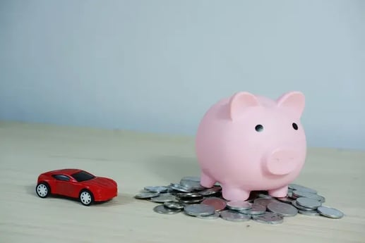 Ahorrar para comprar un carro: alcancía rosada sobre monedas junto a un carro de juguete rojo