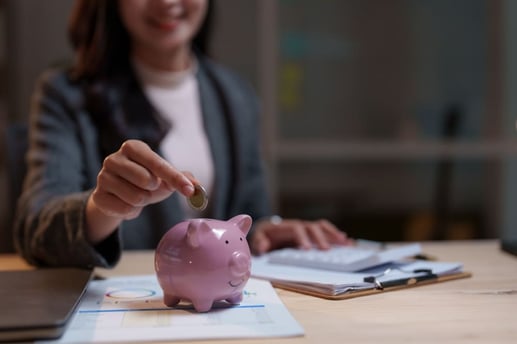 Mujer sonriente guardando una moneda en una alcancía de cerdito para representar las estrategias de ahorro y la creación de un fondo de emergencia seguro.