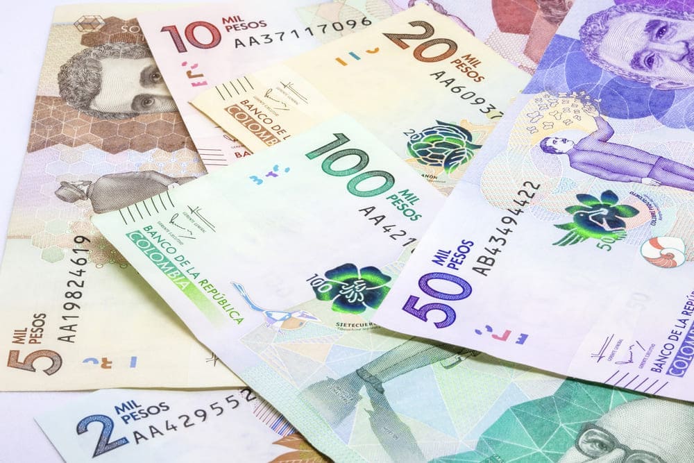 Fajo de billetes de pesos colombianos de diferentes denominaciones sobre una mesa, representando el uso de dinero en efectivo en Colombia.