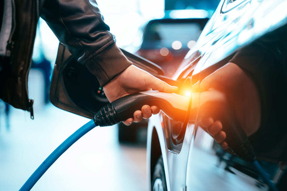 Persona conectando el cable de carga a un carro híbrido enchufable (PHEV) en una estación eléctrica.