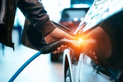 Persona conectando el cable de carga a un carro híbrido enchufable (PHEV) en una estación eléctrica.