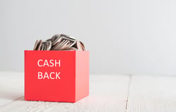 Caja de regalo roja llena de monedas doradas que representa el cashback como recompensa por tus gastos