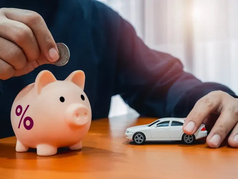 Cómo ahorrar dinero para comprar un carro: mano deposita una moneda en una alcancía con porcentaje junto a un carro