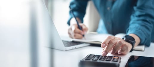 Persona revisando presupuesto diario en calculadora para controlar y eliminar gastos innecesarios.