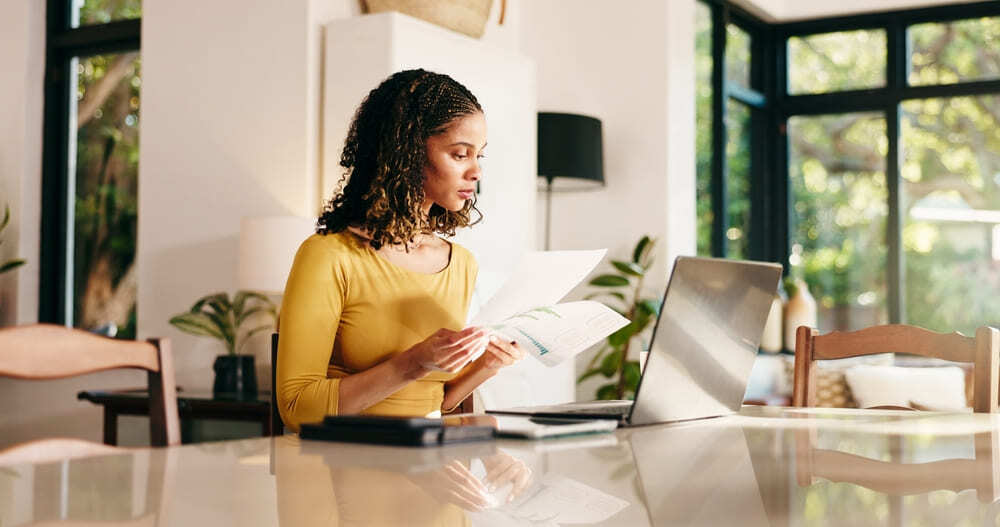 Mujer joven en casa organizando sus finanzas y creando un presupuesto personal en su computadora.
