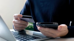 Persona realizando compras electrónicas de forma inteligente sosteniendo una tarjeta de crédito frente a la computadora.