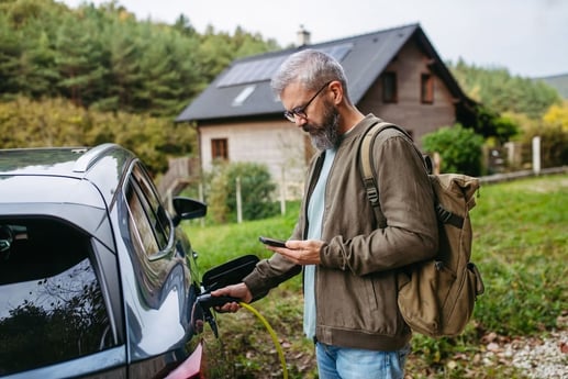 Propietario conectando un carro eléctrico a una estación de carga residencial frente a su casa.