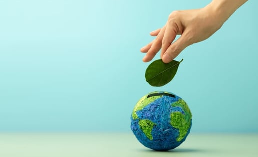 Mano colocando una hoja verde sobre un globo terráqueo, simbolizando el impacto positivo de las finanzas sostenibles.