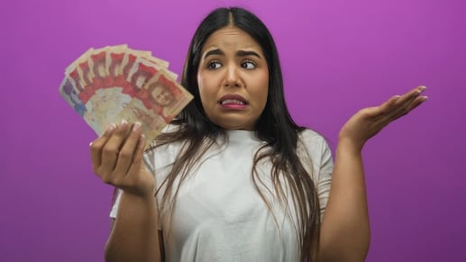 Mujer con expresión pensativa y de duda sosteniendo billetes de pesos colombianos, analizando cuánto dinero se puede portar o retirar en efectivo.