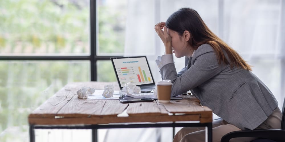 Mujer preocupada frente a su laptop con un café en la mesa, representando el estrés de llegar a fin de mes sin saber en qué se fue el dinero