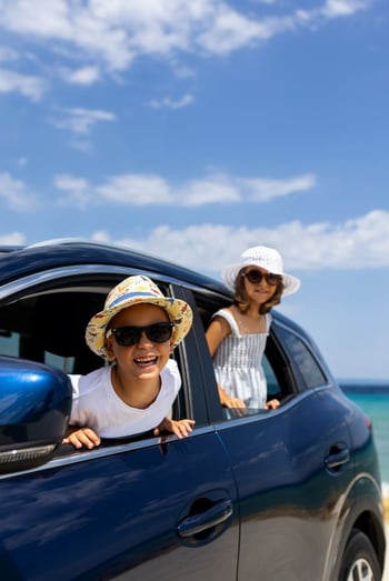 Niños sonrientes asomados por la ventana de un carro azul familiar financiado