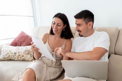 Pareja joven sentada en un sofá revisando su extracto bancario en línea.