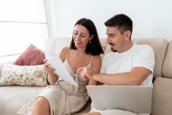 Pareja joven sentada en un sofá revisando su extracto bancario en línea.