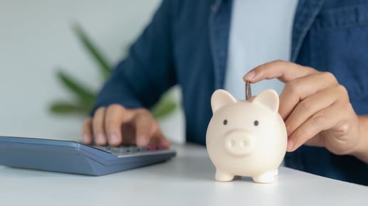 Primer plano de una persona introduciendo una moneda en una alcancía para representar cómo ahorrar dinero en una cuenta bancaria.