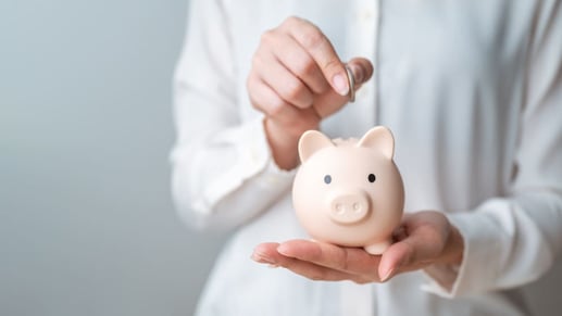 Persona depositando una moneda en una alcancía representando el hábito de ahorro mensual
