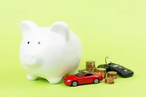 Plan de ahorro para comprar un carro: alcancía blanca, monedas apiladas, llaves y un carro de juguete rojo