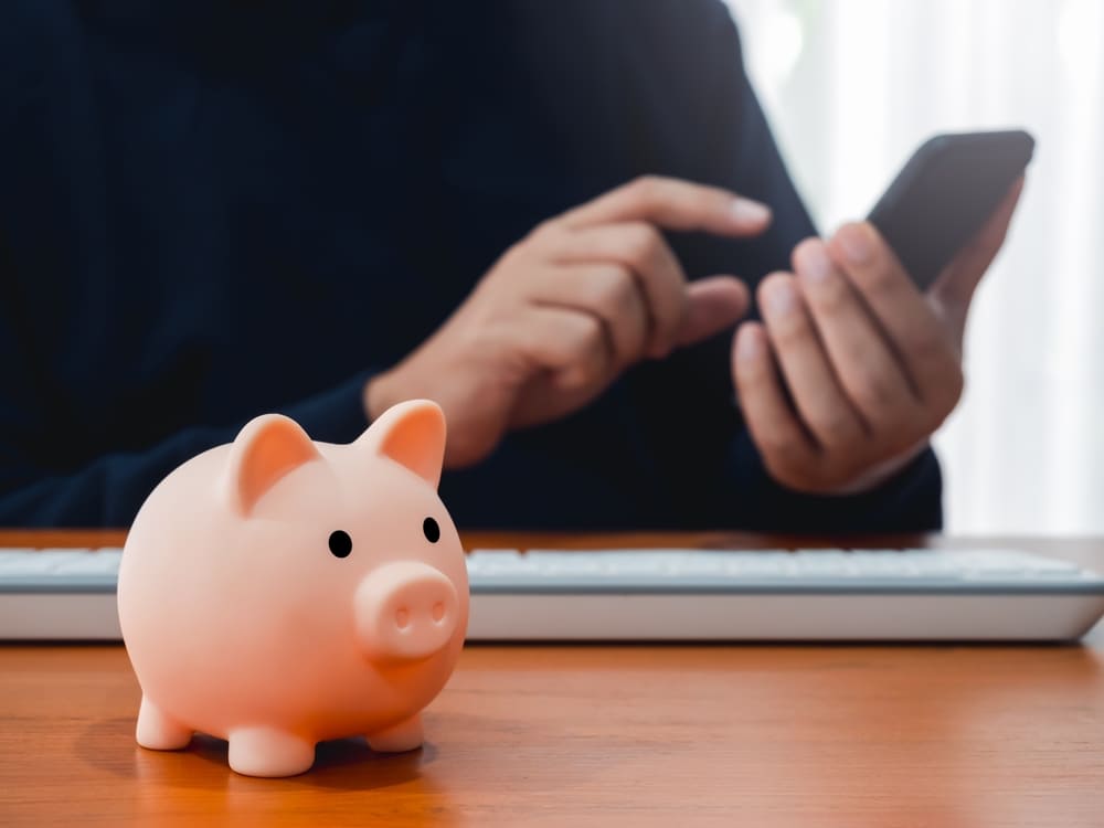 Persona guardando su dinero en cuenta bancaria digital y una alcancía para representar cómo ahorrar dinero en una cuenta bancaria