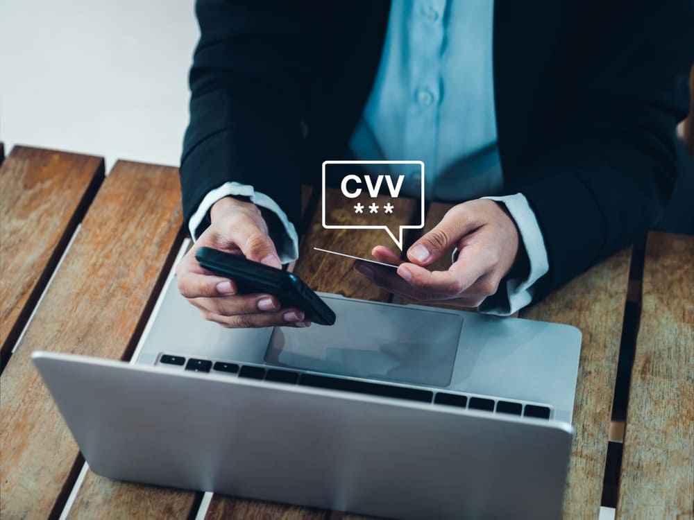 Persona sosteniendo una tarjeta de crédito frente a su computadora portátil para buscar e ingresar el código de seguridad CVV durante un pago en línea.