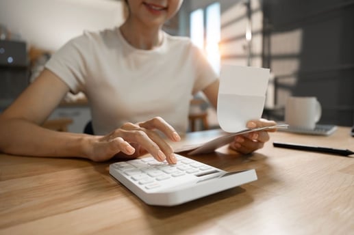 Primer plano de una persona usando una calculadora y revisando un recibo para registrar sus gastos diarios y medir el impacto mensual en su economía