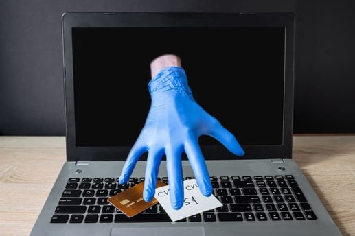 Representación de fraude en línea con una mano saliendo de la pantalla de una laptop para robar una tarjeta de crédito y una nota con el código CVV escrito.