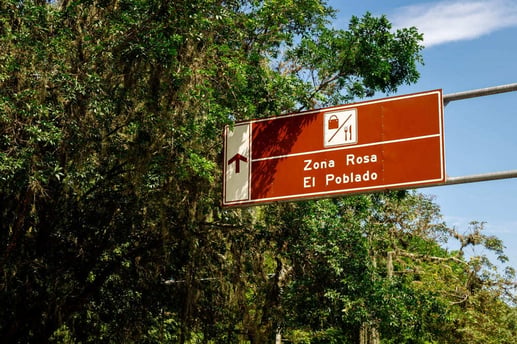 Señal de tránsito informativa de turismo color marrón que indica la dirección hacia la Zona Rosa y El Poblado en Medellín, Colombia.
