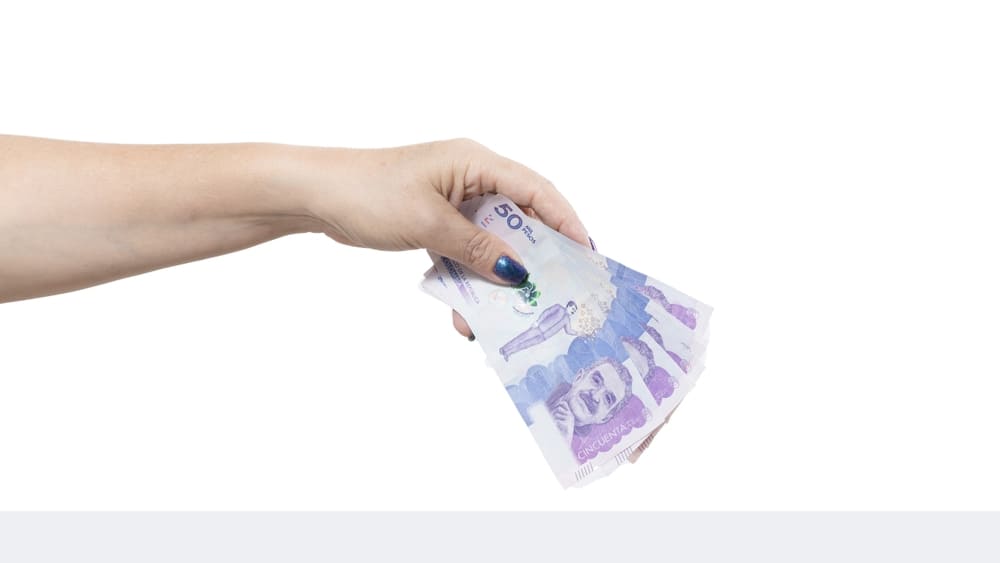 Mano de una mujer sosteniendo billetes de pesos colombianos, ideal para ilustrar opciones seguras de ahorro y cómo guardar dinero en el país.