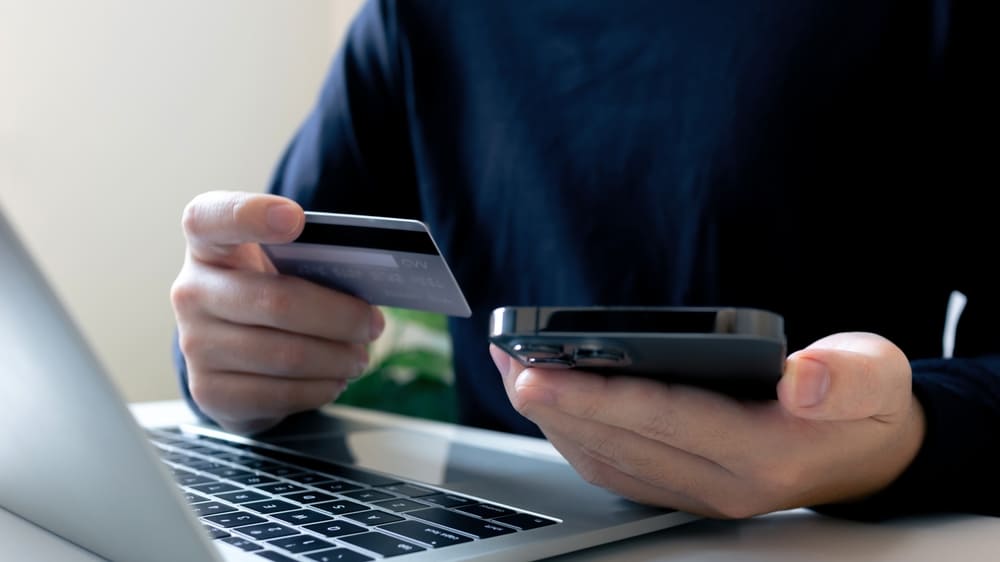Persona realizando compras electrónicas de forma inteligente sosteniendo una tarjeta de crédito frente a la computadora.