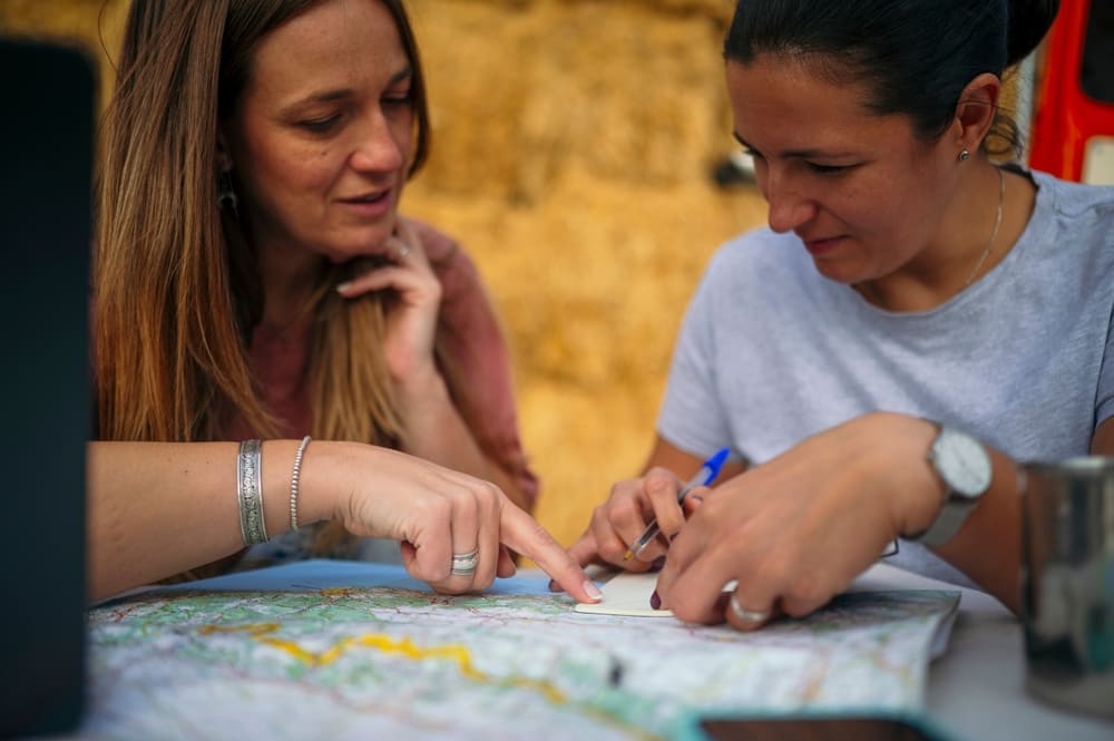 Dos personas organizando un presupuesto de viaje con mapa, libreta y computador portátil